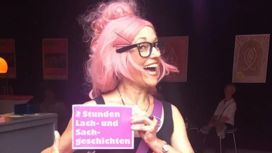 Smiling person holds sign, pink wig, indoor setting.