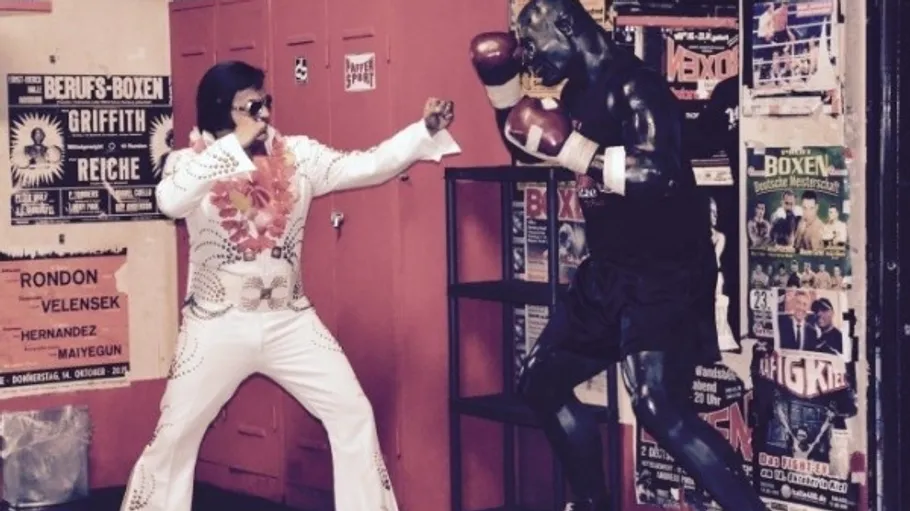 Mann in Kostüm posiert mit Boxermannpuppe.