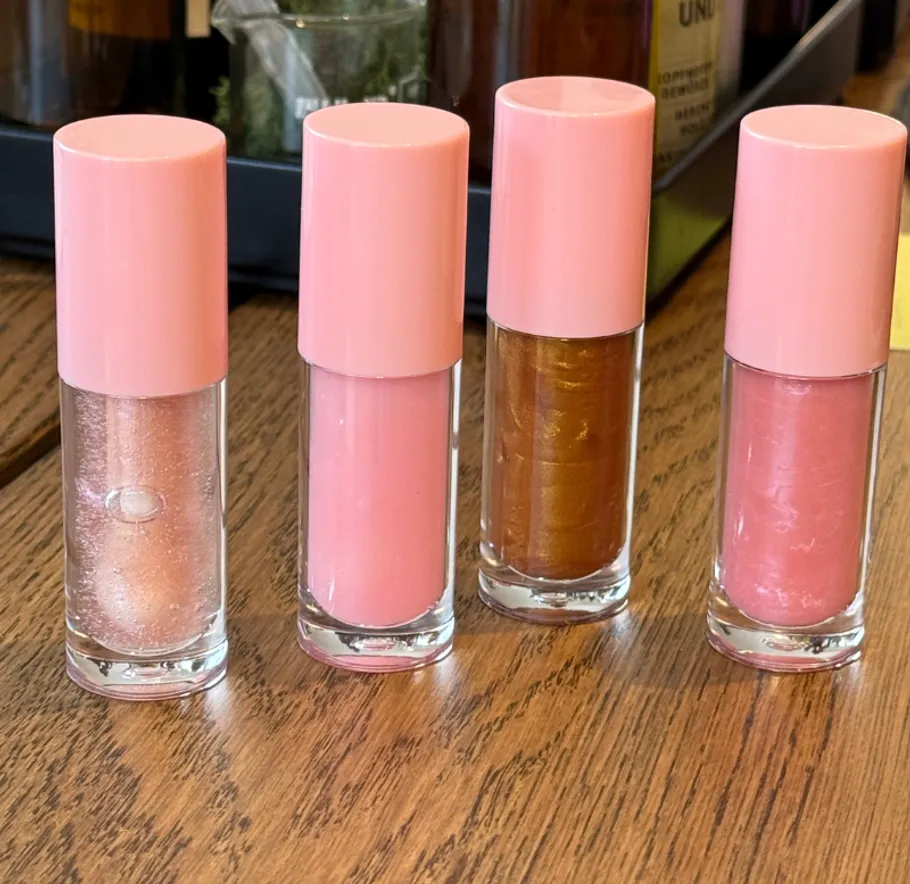 Four lip glosses with pink caps on table.