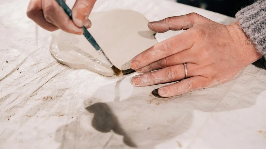 Hands shaping and painting clay on a table.