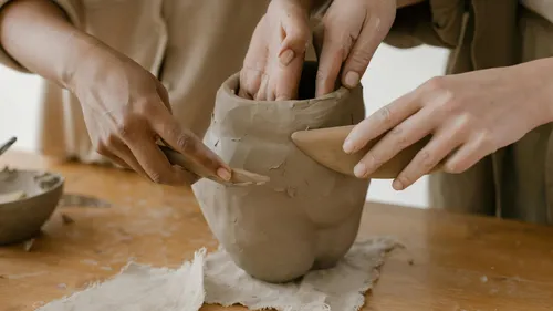 Hands sculpting clay vase on wooden table.
