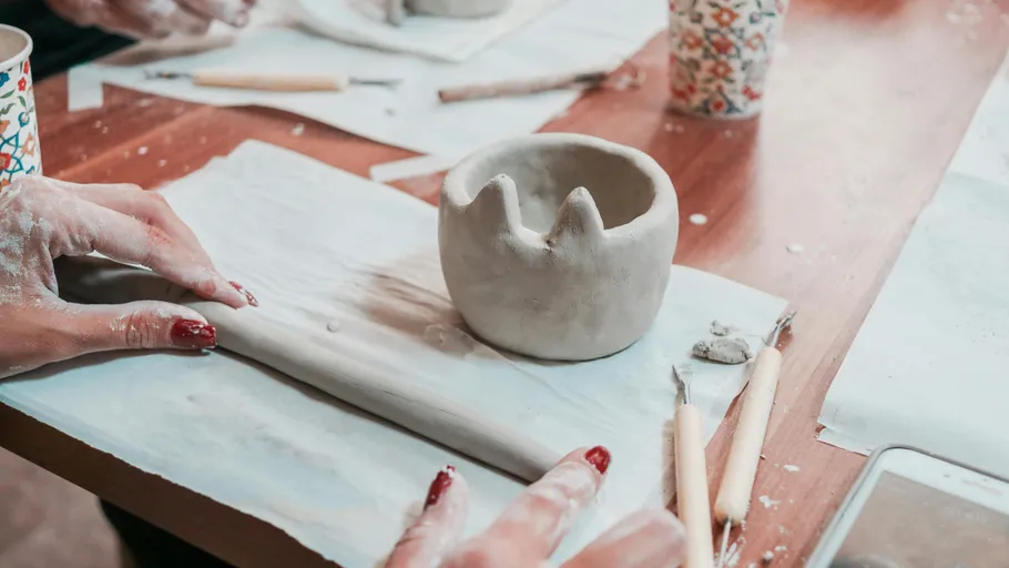 Hands shaping clay on a wooden table.
