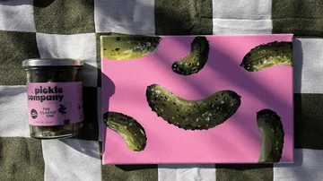 Gurkenglas und Gemälde auf kariertem Tuch.
