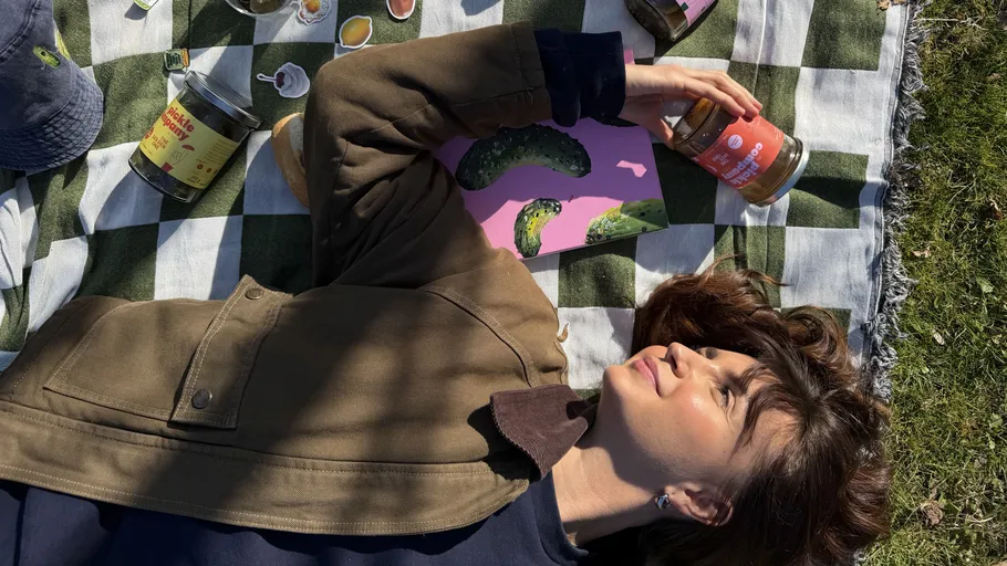 Woman laying on blanket holding a jar outside.