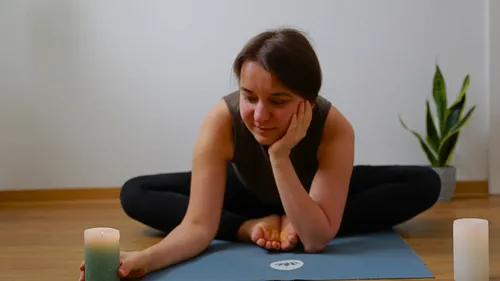 Woman in yoga pose with candles on mat.