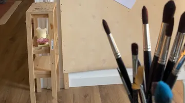 Pinsel im Fokus, Holzschemel im Hintergrund.