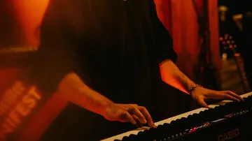 Person playing keyboard under orange lighting.