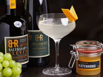 Cocktailglas mit Getränk, umgeben von Ginflaschen und Honig.