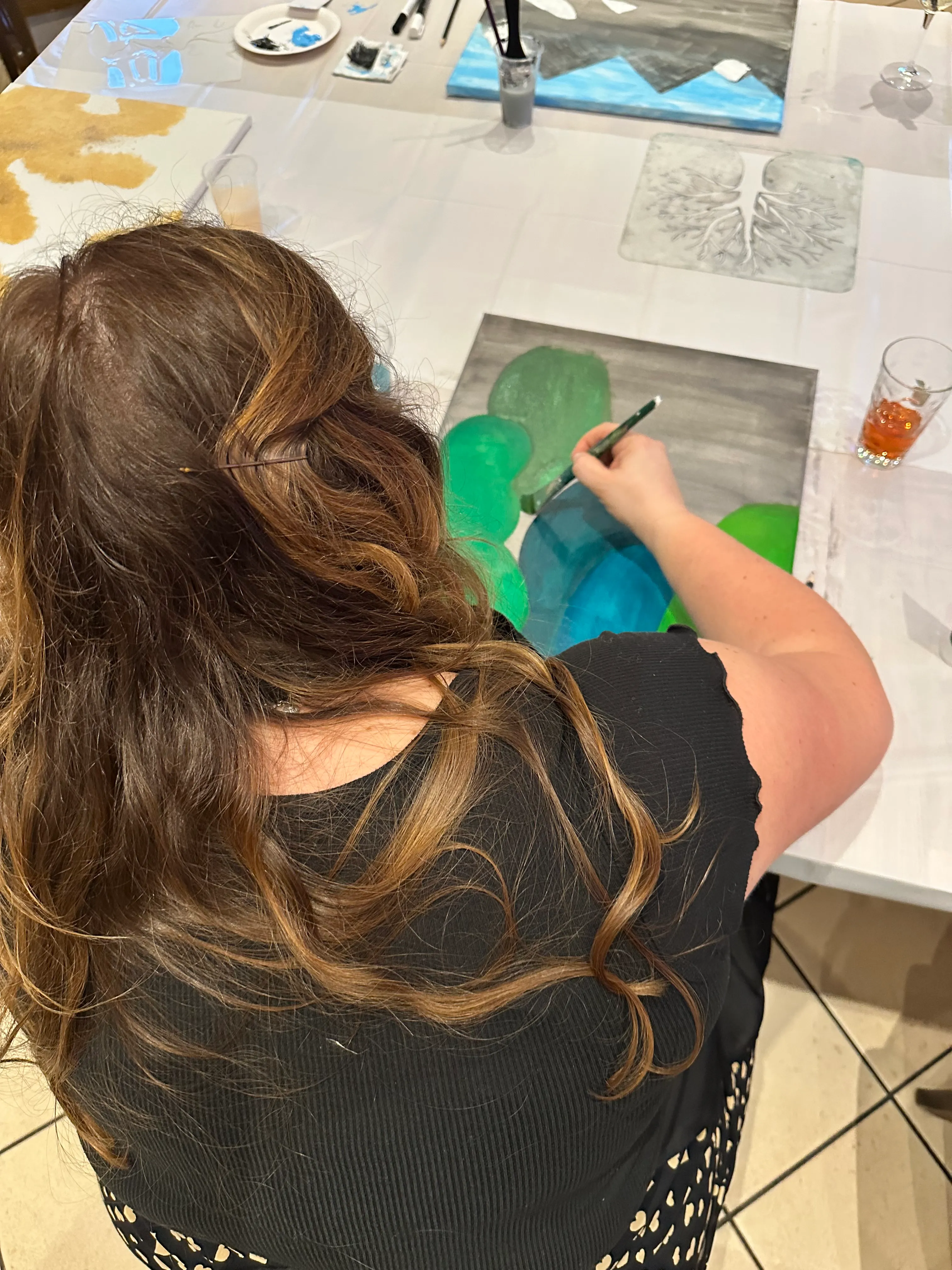 Frau malt an einem Tisch, Getränke in der Nähe.