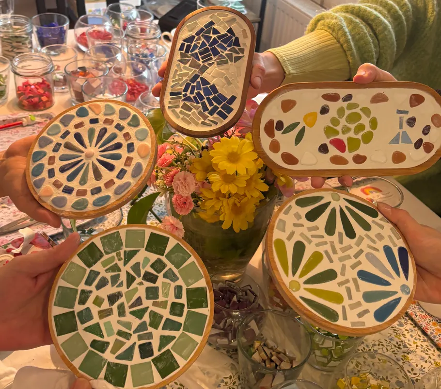 Hands holding colorful mosaic trays, flowers in background.