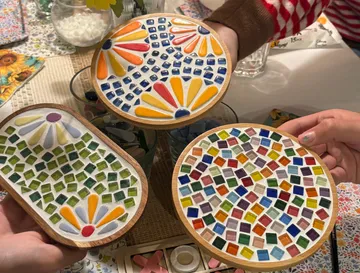 Hands holding colorful mosaic trays and coasters.
