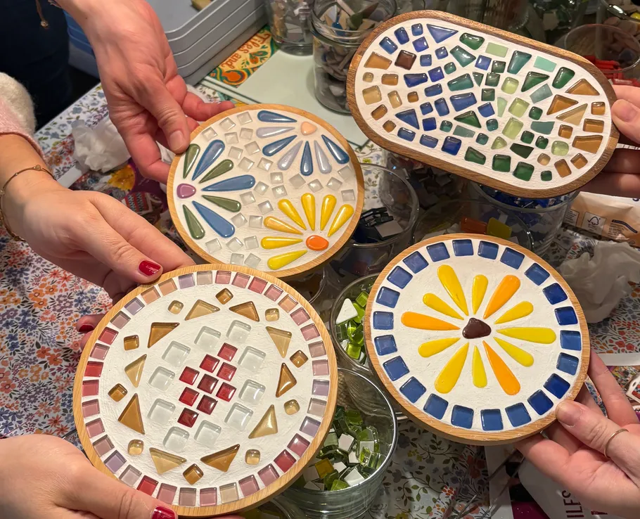 Hände halten bunte Mosaik-Untersetzer auf Tisch.