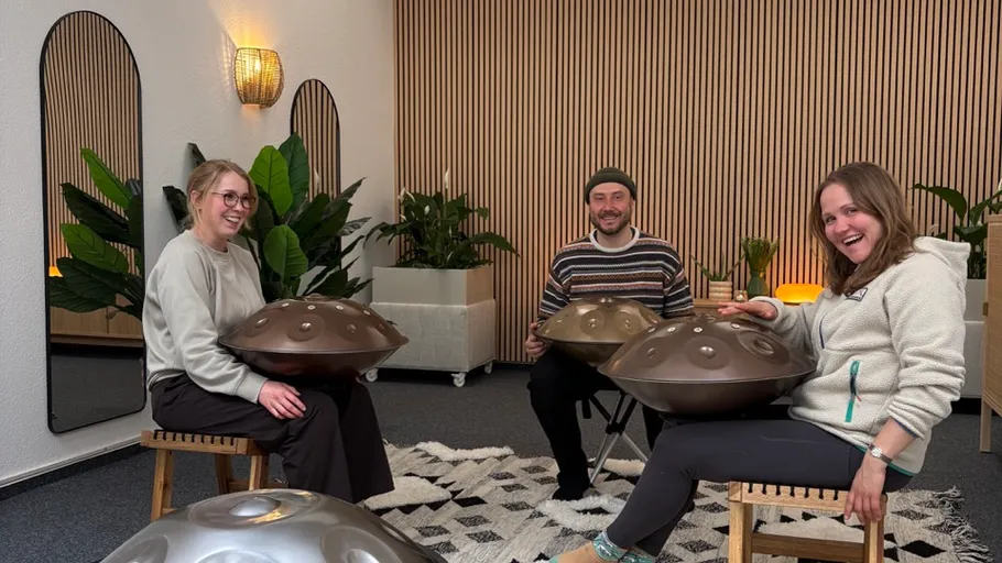 Three people playing handpans in a cozy room.