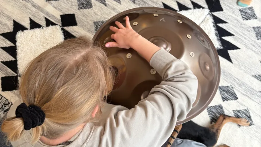 Person playing handpan indoors on patterned rug.