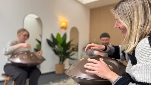 Menschen spielen Handpans in gemütlichem Raum.