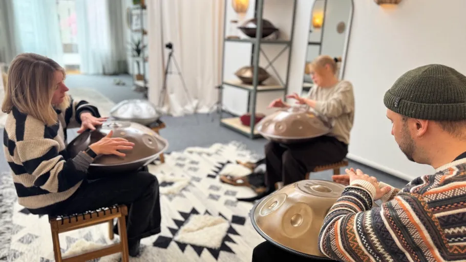 Drei Personen spielen Handpans in gemütlichem Raum.