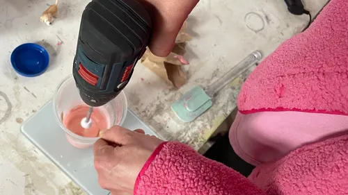 Person mischt rosa Flüssigkeit mit Bohrer im Becher.