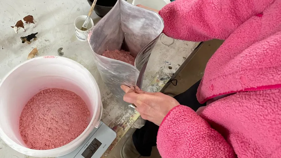 Person pouring pink powder into a bag.