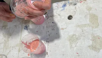 Hände gießen pinke Flüssigkeit in Becher auf Tisch.