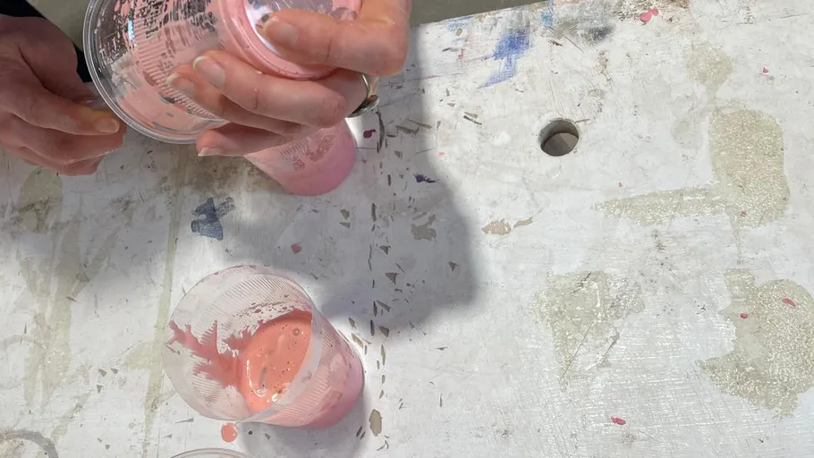 Hands pouring pink liquid into cups on table.