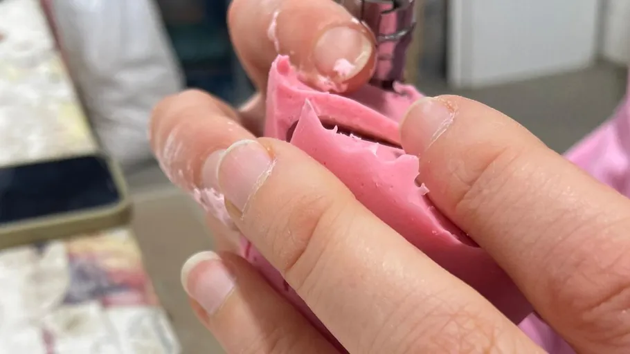 Hände formen rosa Material mit einem Werkzeug.