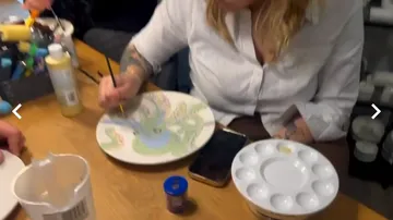 Frau bemalt Teller an einem Holztisch.
