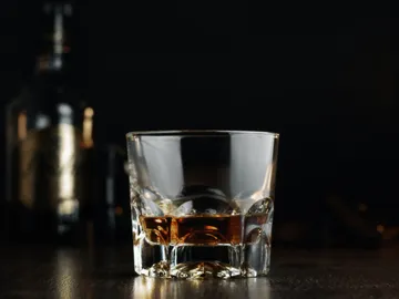 A glass of whiskey is on a dark table.