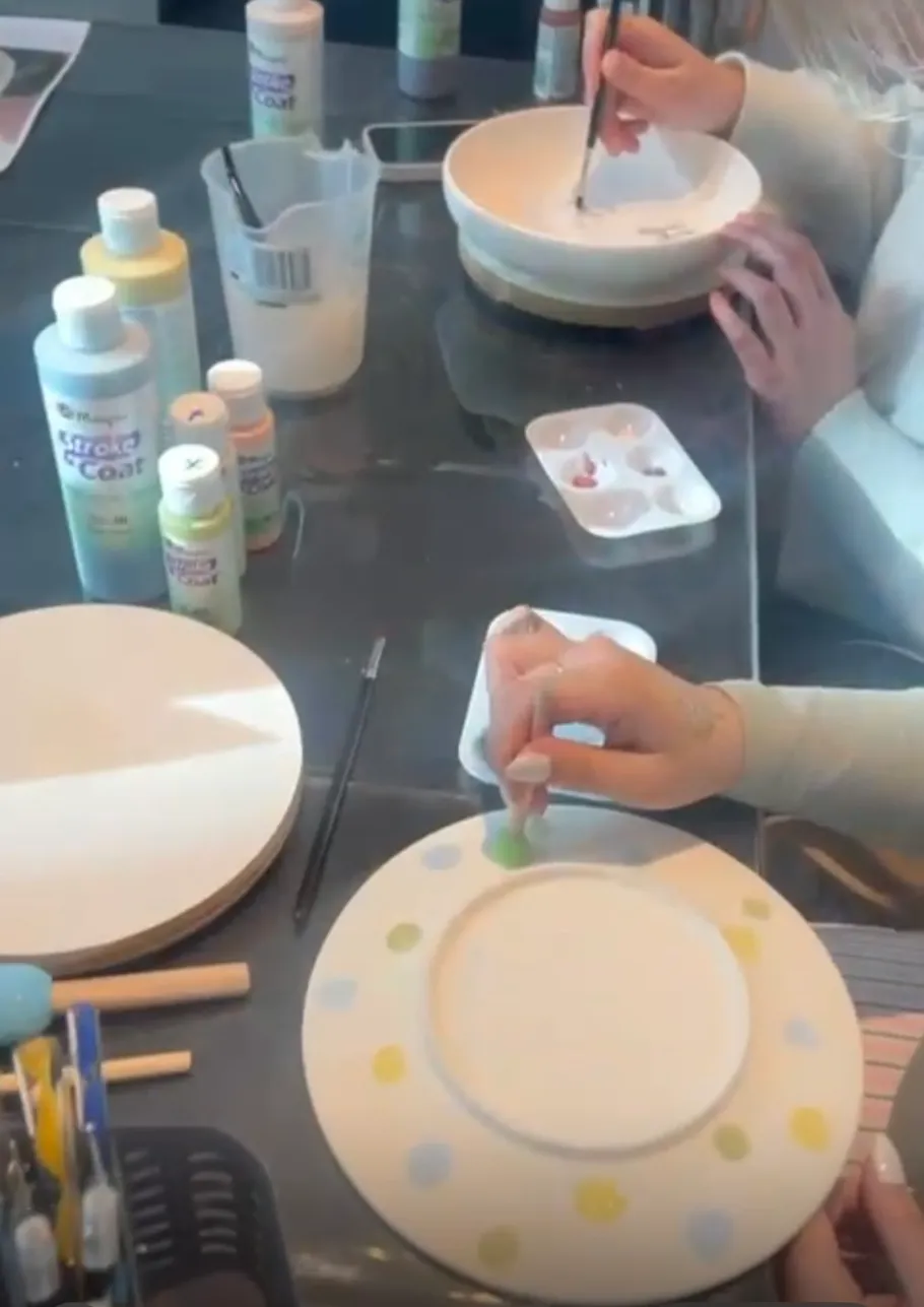 Person painting pottery with colorful dots, tools nearby.