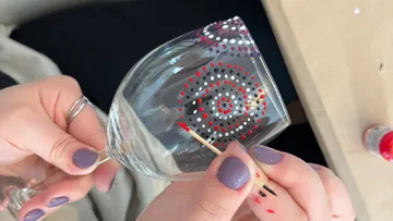 Person bemalt Glas mit bunten Punkten.