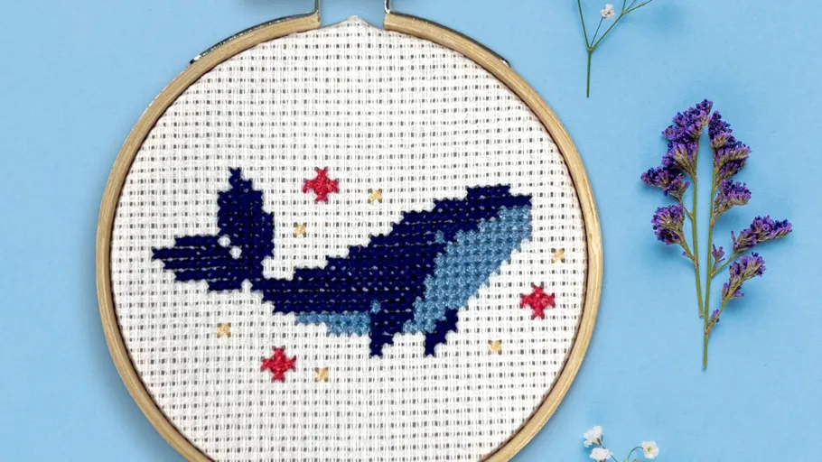 Cross-stitched whale with stars in a hoop.
