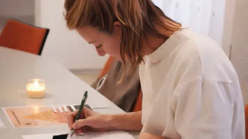 Woman writing at a table with candle.