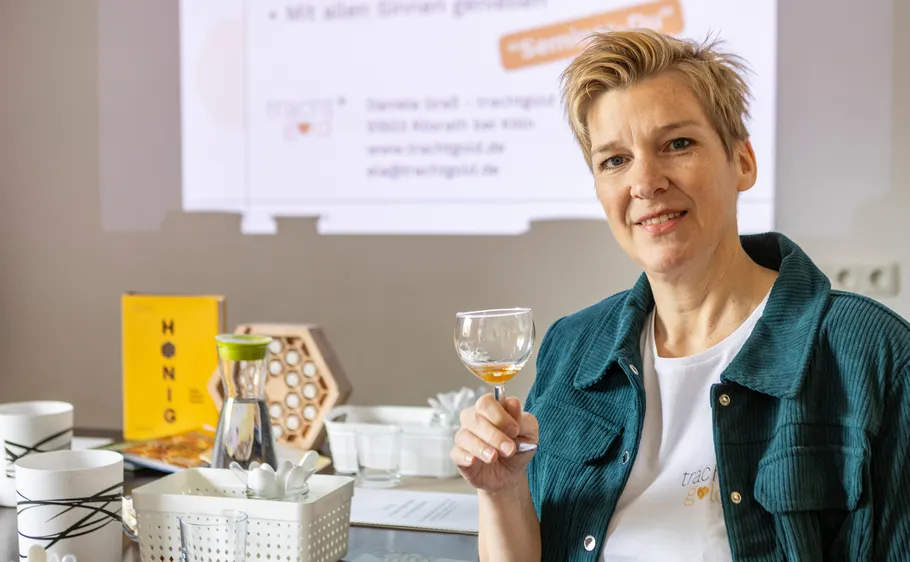 Person hält Glas am Tisch mit Honigprodukten.