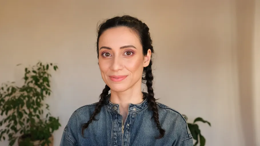 Woman with braids smiling indoors, plants behind.
