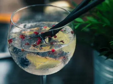 Ein Glas mit Getränk, Kräutern und Pfefferkörnern wird gerührt.