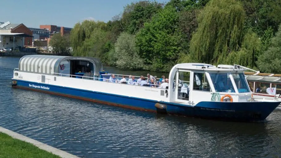 Ausflugsboot fährt entlang grüner Flussufer.