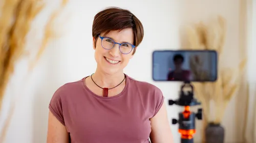 Frau lächelt mit Brille neben einem Stativ.