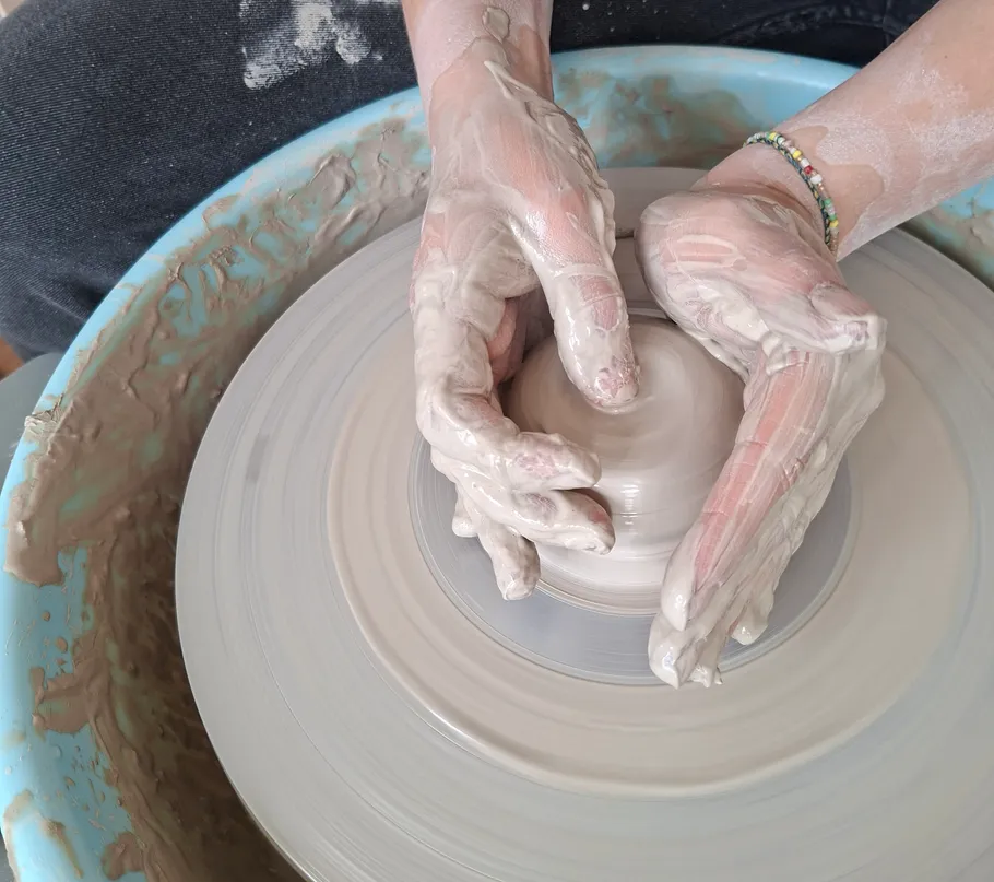 Hands shaping clay on pottery wheel.