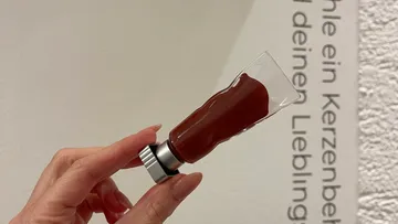 Hand holding a brown candle sample indoors.