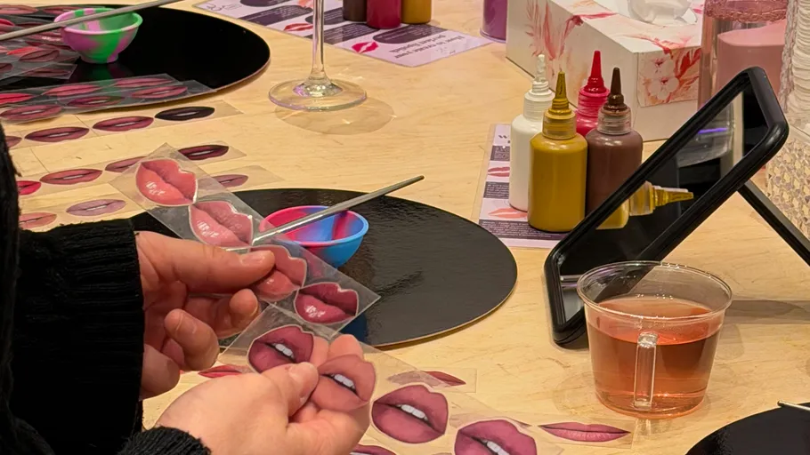 Person hält Lippenfarbmuster an Schminktisch.