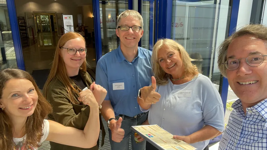 Group of five people smiling and gesturing thumbs up.