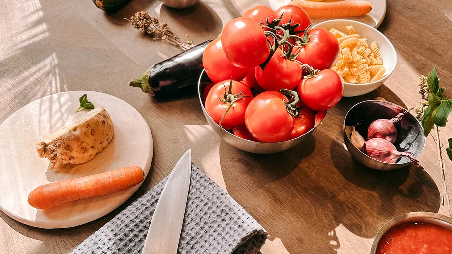 Tomatoes and vegetables on wooden kitchen table.