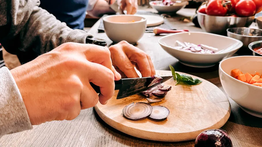 Person slicing red onion on wooden board.