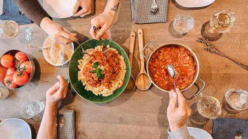 People serving pasta with tomato sauce at table.
