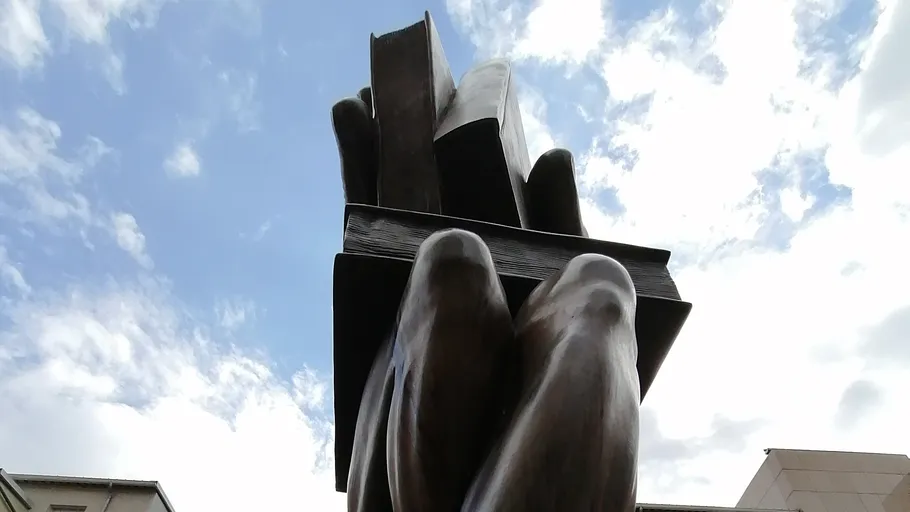 Sculpture of hands holding books outside.