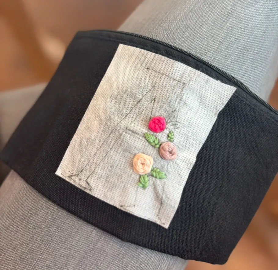 Embroidered flowers and letter on black cloth.