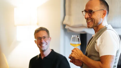 Two men smiling and holding a drink indoors.