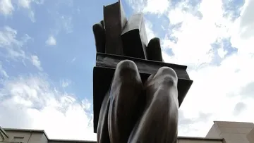 Sculpture of hands holding stacked books outdoors.