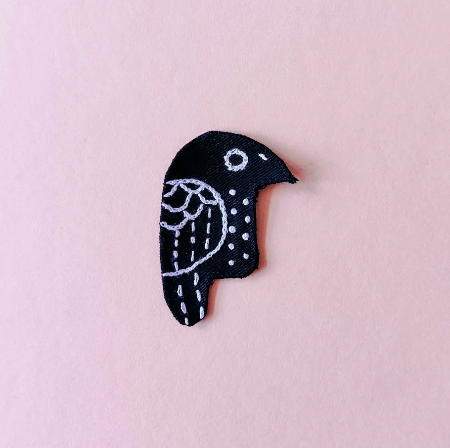 Schwarzer Vogelstickerei auf rosa Hintergrund.