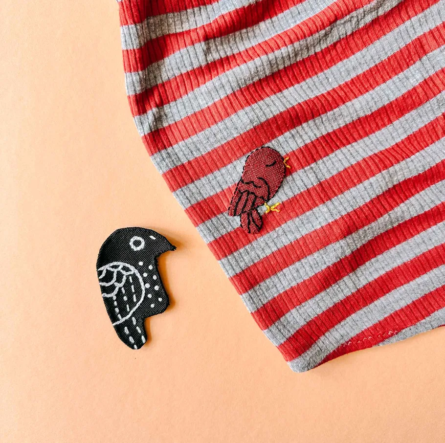 Embroidered red bird on striped fabric.