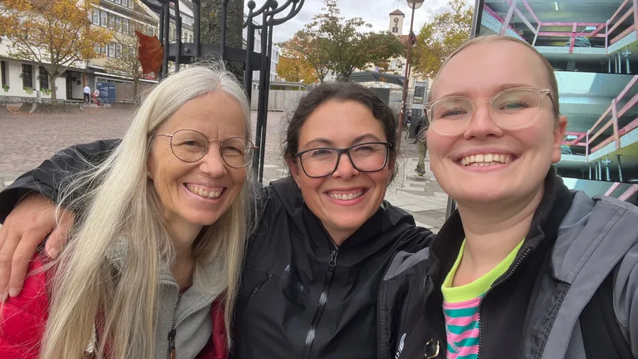 Three people smiling outdoors in urban setting.